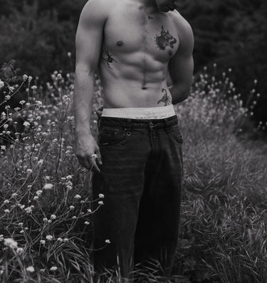 Man with tattoos standing in a field of wildflowers and grass.