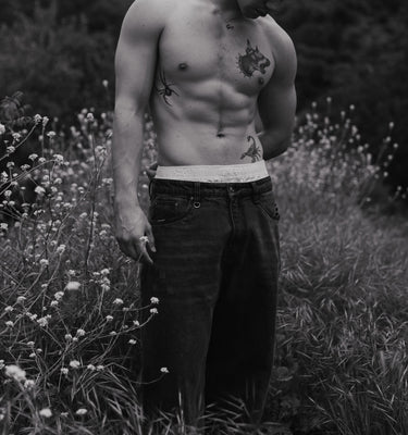 Man with tattoos standing in a field of wildflowers and grass.