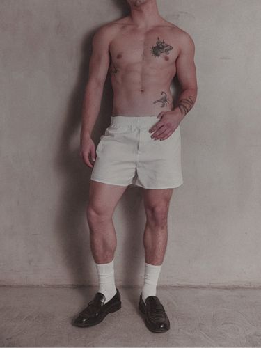 Man wearing white shorts and black shoes against a plain wall